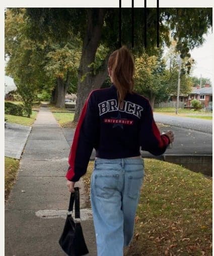 The back of a navy Brock University crewneck, worn down a tree-lined street